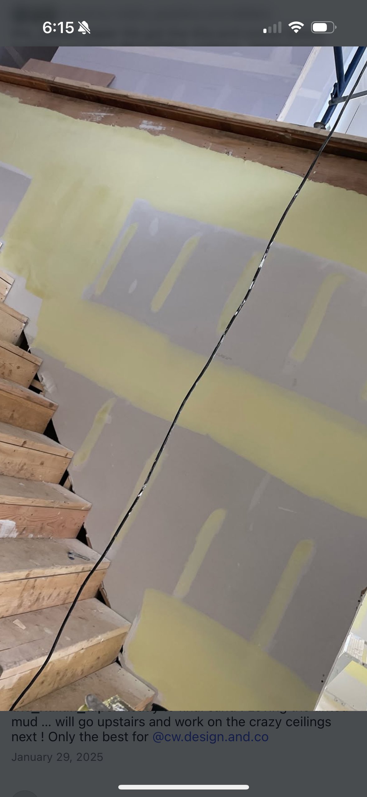 Interior drywall installation with yellow insulation and wooden framing visible on ceiling under construction